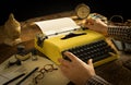 ManÃ¢â¬â¢s hands typing on a vintage yellow typewriter on an wooden desk